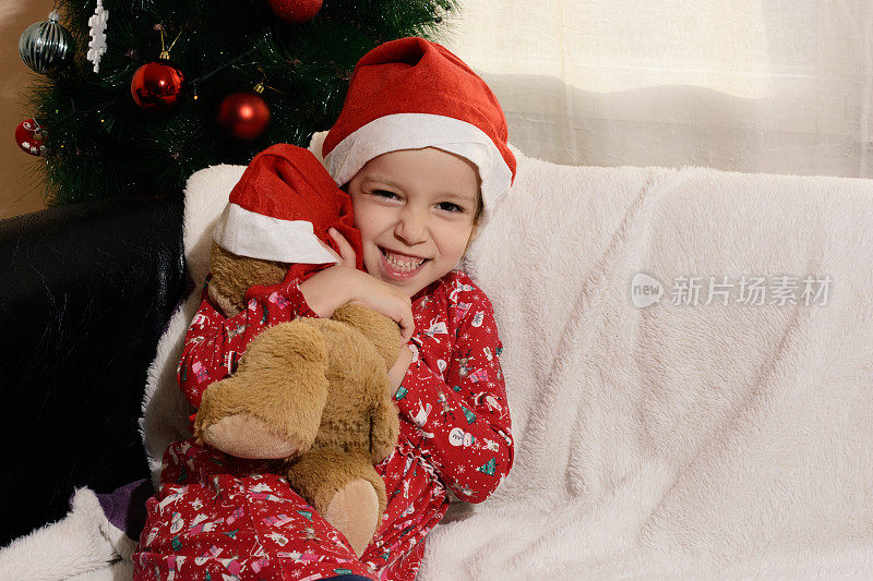 一个孩子在圣诞树前抱着她的泰迪熊