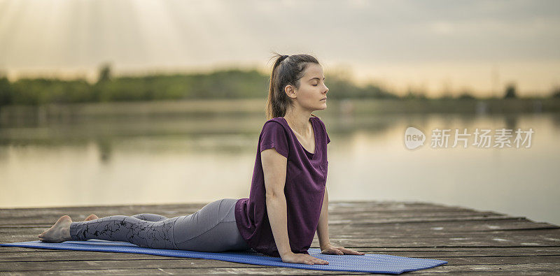 年轻女子练习瑜伽，做向上面对狗运动，乌尔德瓦穆哈什瓦纳体式在湖码头