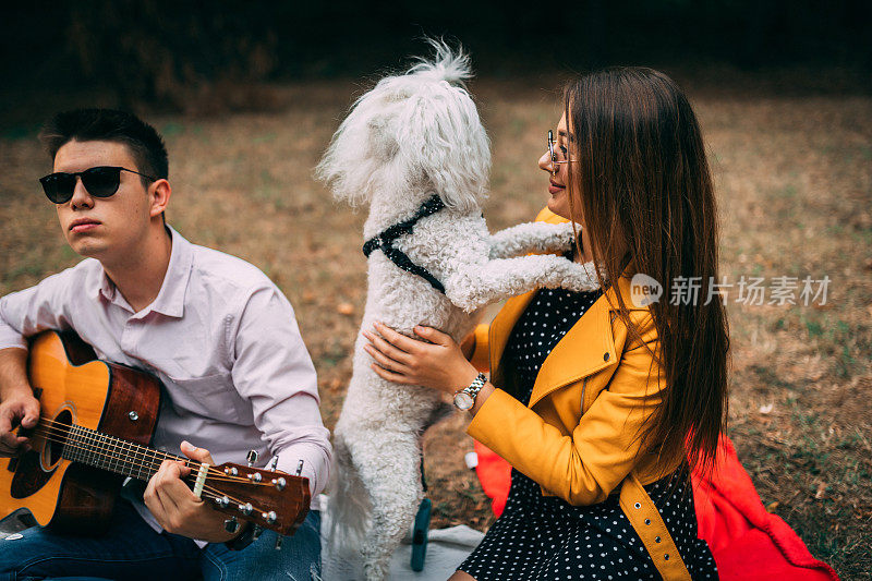 十几岁的男孩和十几岁的女孩与白色狮子狗野餐