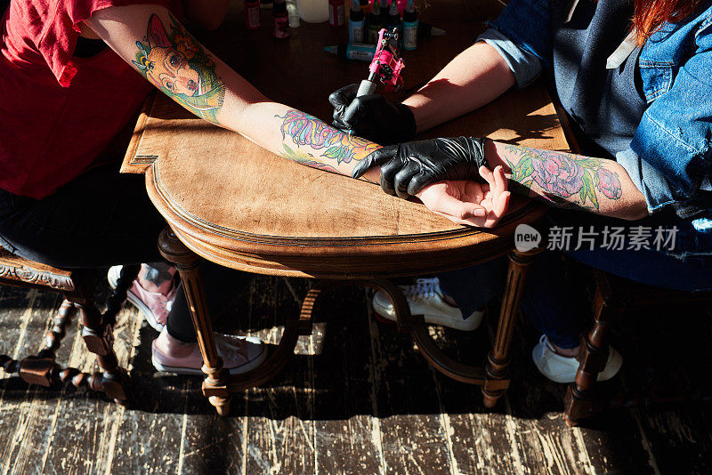 高角度的年轻女子在专业纹身工作室的手臂上进行彩色纹身，精通电动纹身机的工作