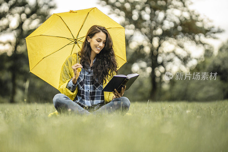 年轻女子穿着黄色雨衣，撑着黄色雨伞，在户外看书，享受雨中的乐趣