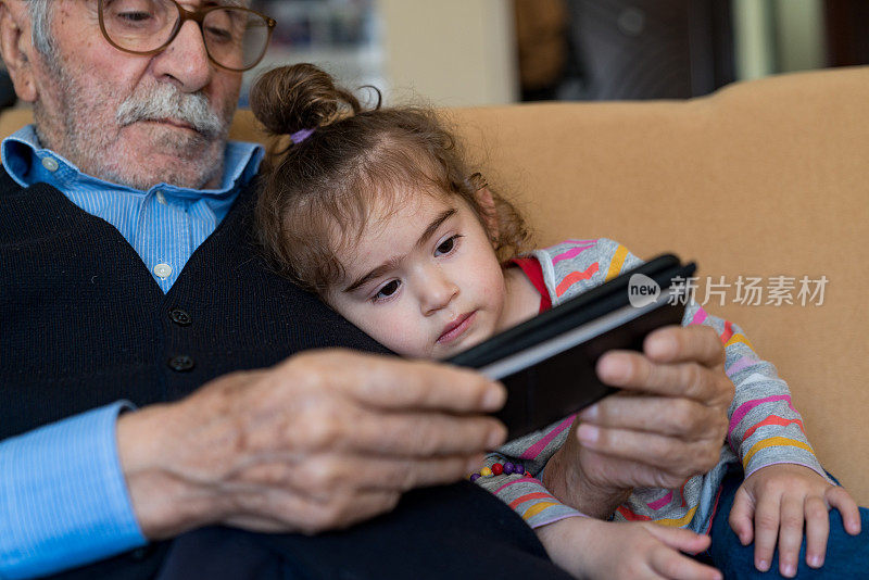 爷爷和孙女坐在沙发上使用智能手机