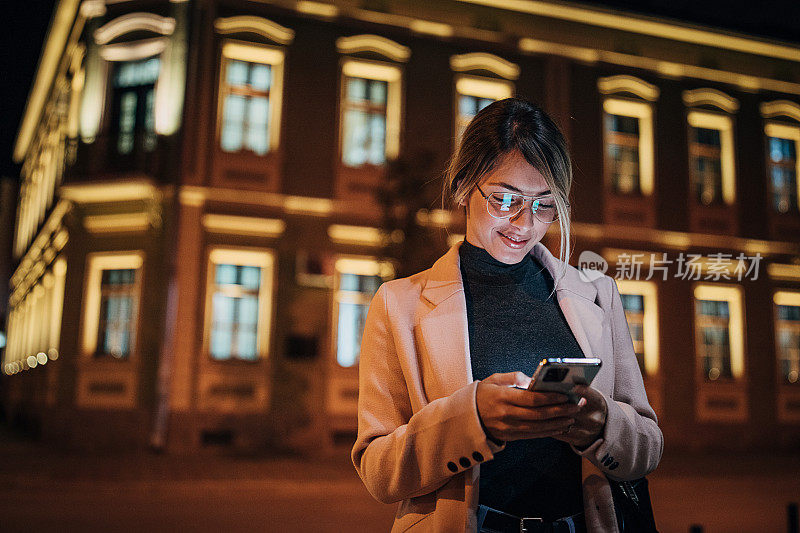 一个女人晚上站在城市街道上玩手机