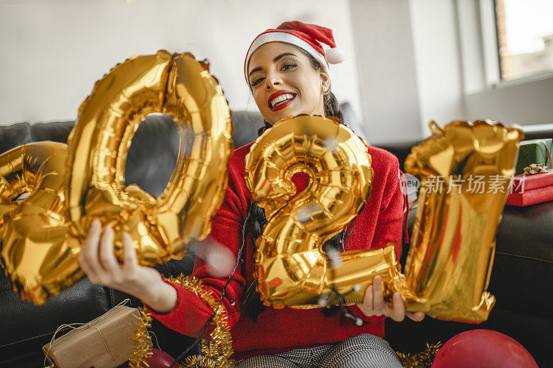 一名年轻女子在新年派对上玩得很开心，手里拿着写有“2021”的气球，代表即将到来的新年