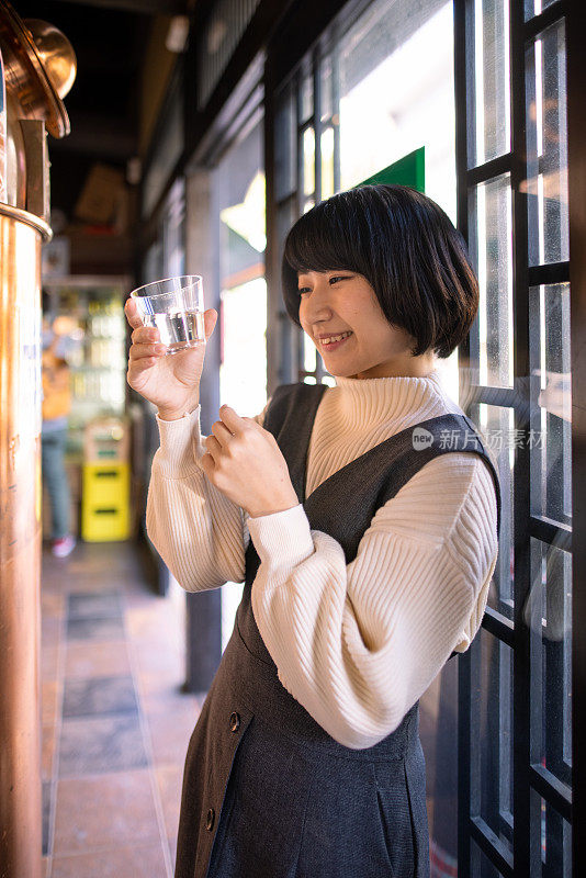 在传统的日本温泉区，快乐的年轻女子拿着一杯“saki”(日本米酒)