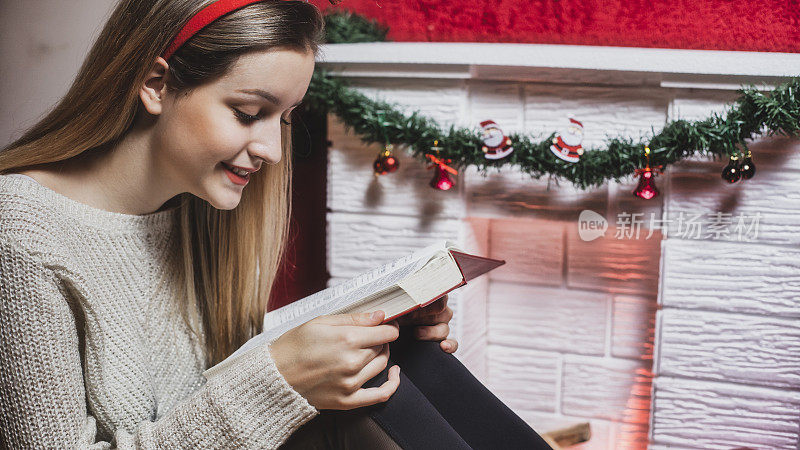 年轻女子在圣诞树下看书，在壁炉旁暖腿