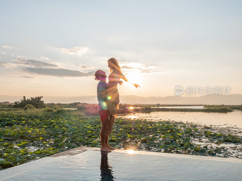 一对夫妇在泳池边，女人在伴侣的怀抱中跳跃