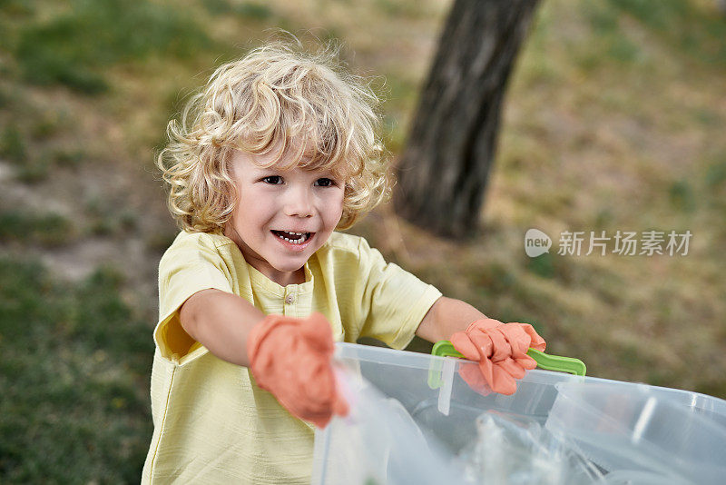 可爱的小男孩戴着橡胶手套拿着回收箱，微笑着和父母在森林或公园里收集塑料垃圾