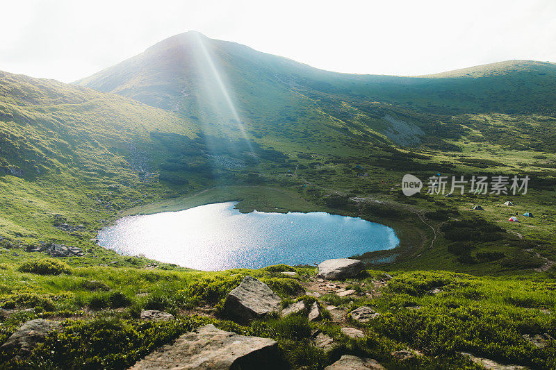 夏日日落时分，一群人在山湖上搭帐篷露营