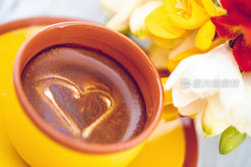 近距离的黄色杯与奶油咖啡与爱的心在框架内的小苍兰