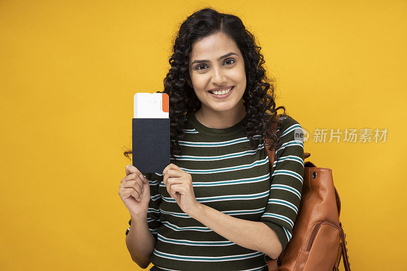 年轻女学生的肖像显示机票和护照站在黄色背景孤立