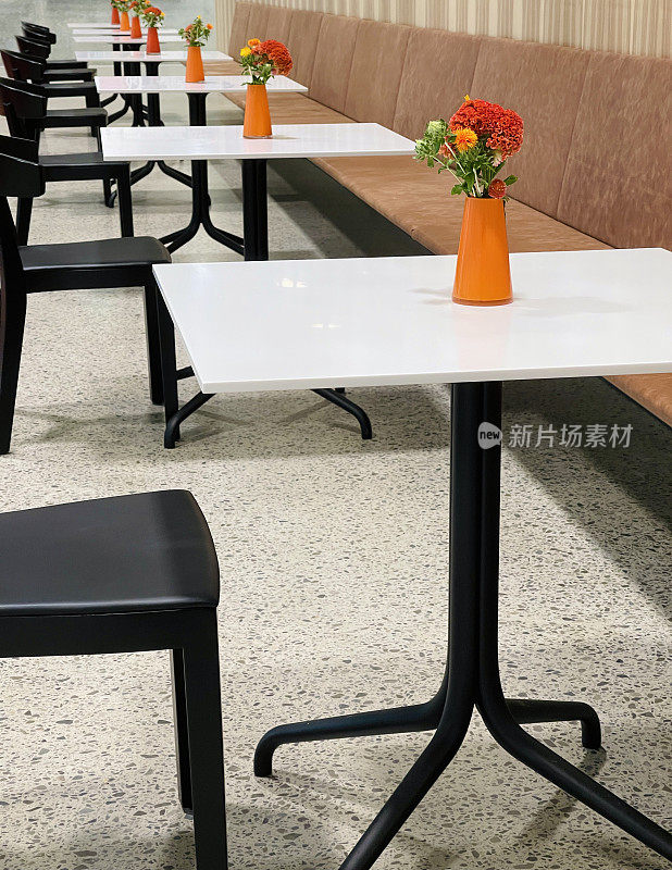 一排咖啡桌，每一张桌上都有一束装在橘色花瓶里的花