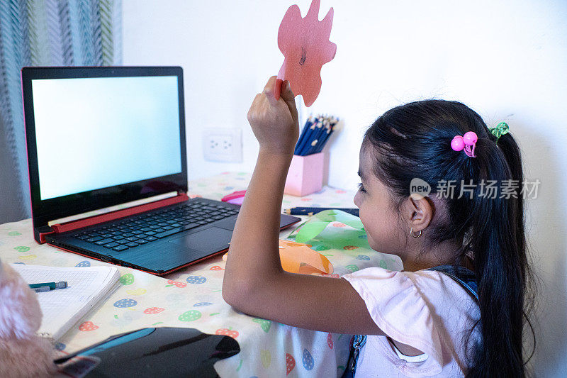 一个小女孩在家里用笔记本电脑进行facetime视频通话，使用在线虚拟课堂缩放
