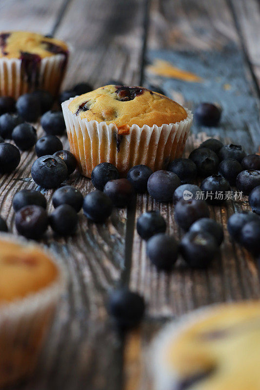 图片批新鲜烘焙的蓝莓松饼在纸蛋糕盒周围的新鲜蓝莓，木纹背景