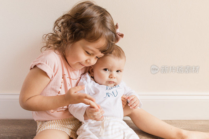 一个3岁的蹒跚学步的小女孩抱着她4个月大的弟弟，同时穿着“大姐姐”和“小弟弟”的衬衫