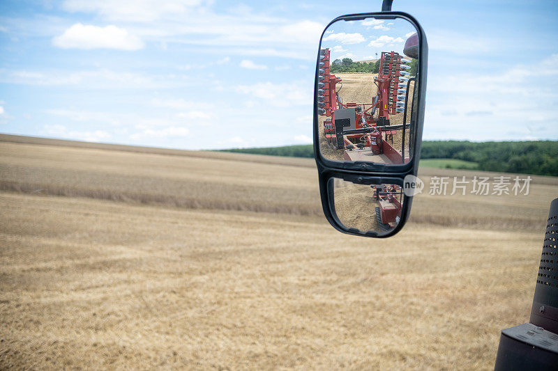 从拖拉机的窗口看到的农田。在拖拉机的镜子里，可以看到附带的设备。