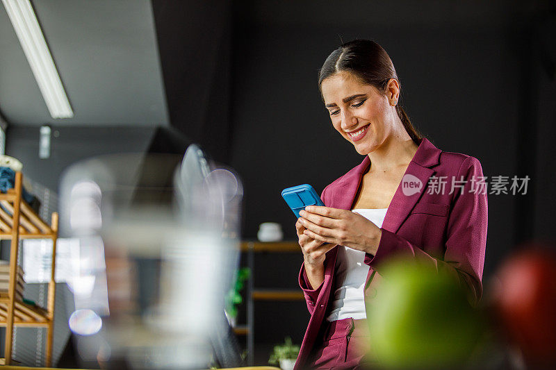年轻的女商人坐在她的桌子边，通过智能手机回复短信