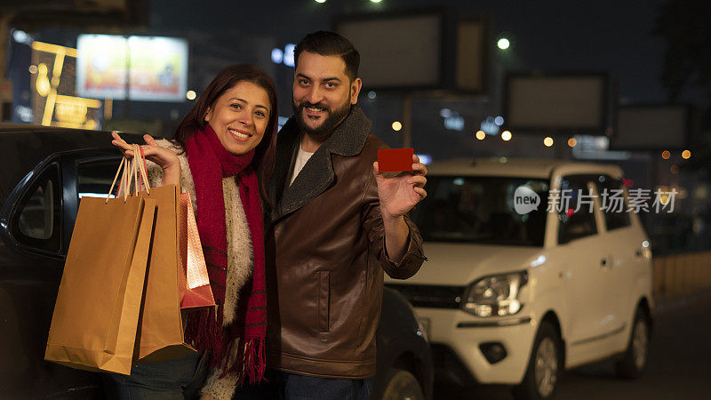 幸福的年轻夫妇在晚上购物袋和显示信用卡