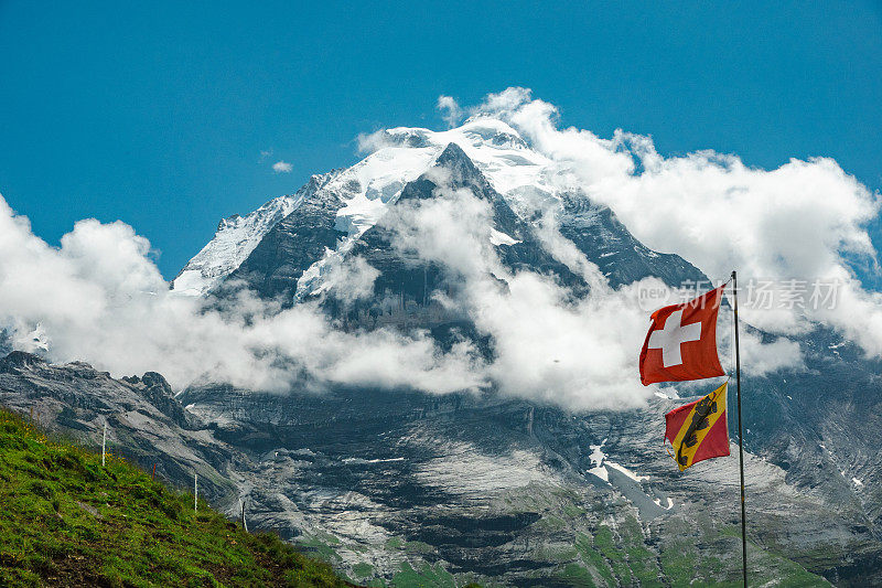 瑞士伯尔尼亚斯高山的荣格弗劳山峰顶。山顶部分在云层中。前景是伯尔尼州和瑞士的国旗。