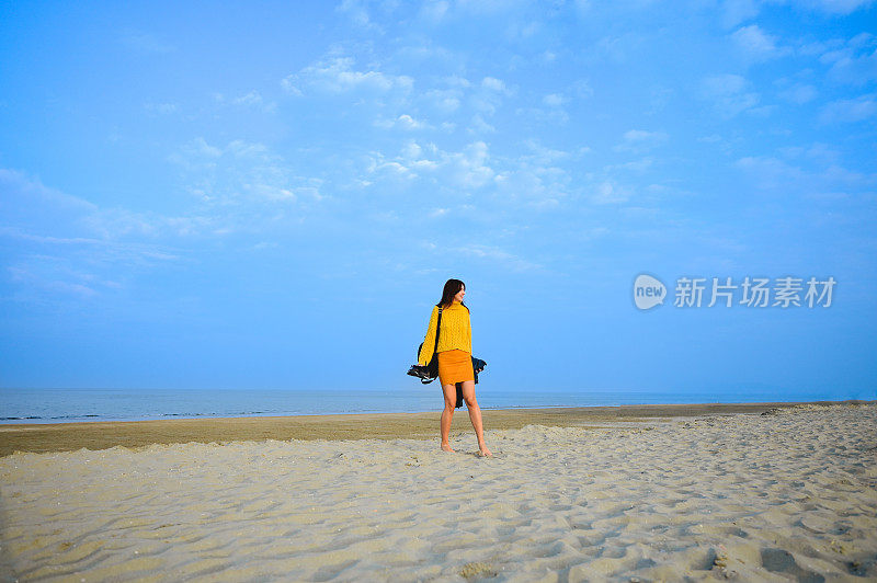 女人穿着黄色保暖的衣服，走在海边的沙滩上。