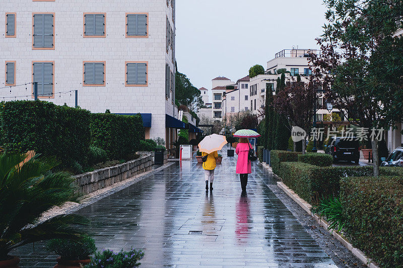 后面的女人，穿着鲜艳的布，打着伞，在雨中走着