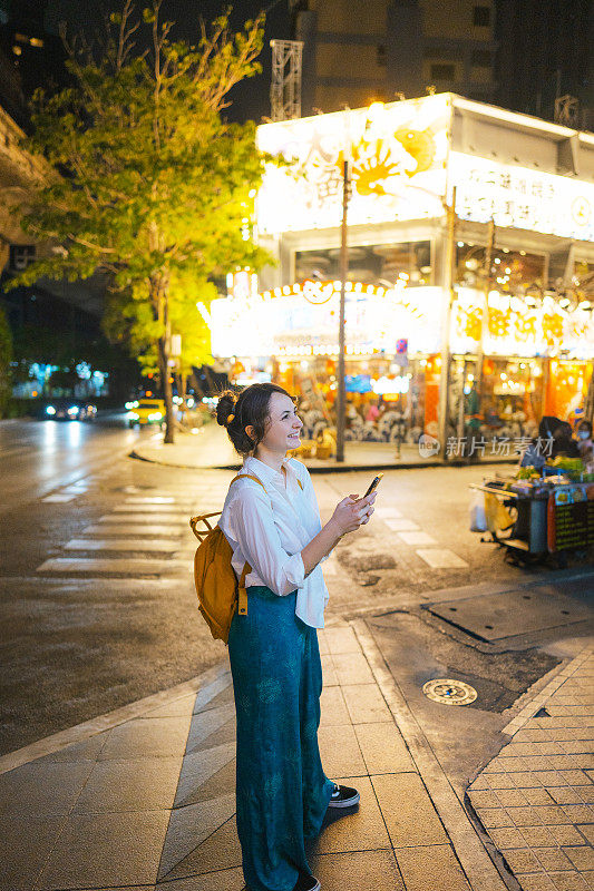 一个拿着智能手机的女人晚上走在城市里