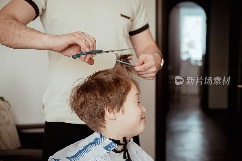 在隔离条件下的美发沙龙。父亲用剪刀给儿子剪头发。男人在家里给男孩理发。经济危机中的经济概念。