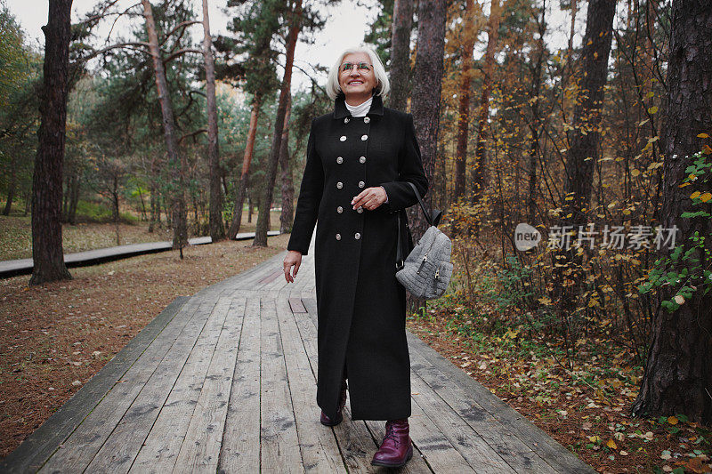 快乐的老妇人，满头银发，带着美丽的笑容，漫步在森林里的自然公园里，享受着自然之美，真诚率真的时刻