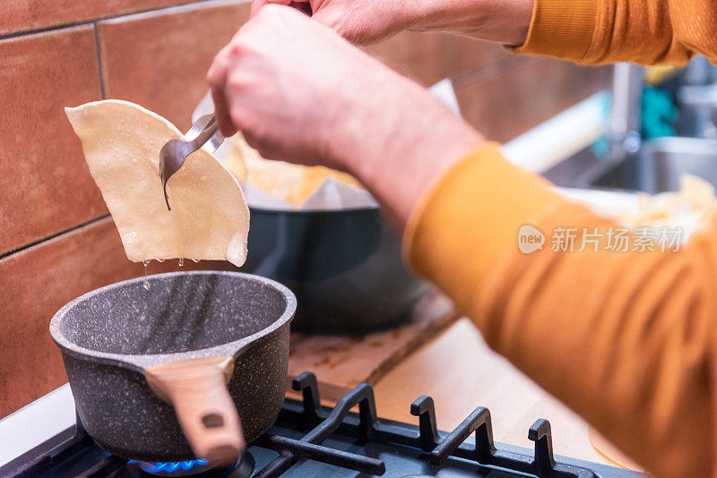 一个成熟的男人在家里的厨房里煎着传统的印度小吃——帕帕多姆