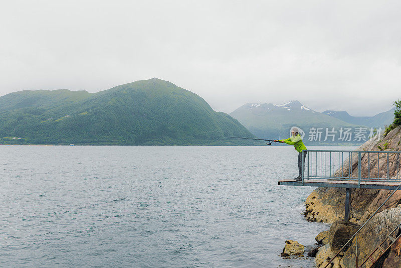 身穿绿夹克的女子在挪威峡湾钓鱼