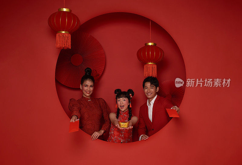 幸福的亚洲家庭穿着传统的旗袍旗袍，拿着红色装饰背景上的红包。