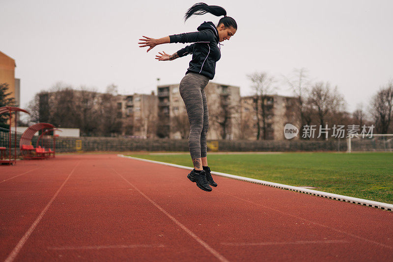 一位年轻的健身女士正在跑道上热身。她跳。