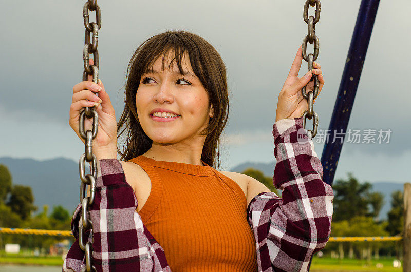 美丽的年轻女子穿着休闲服在公园荡秋千的肖像