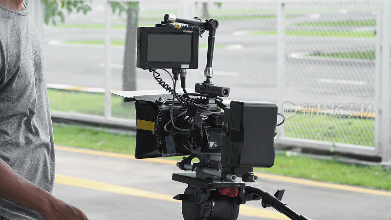 高清晰度数码摄像机的背角视图，记录或拍摄电视商业生产在平移倾斜移位专业头三脚架在户外位置和电影摄制组与设置。