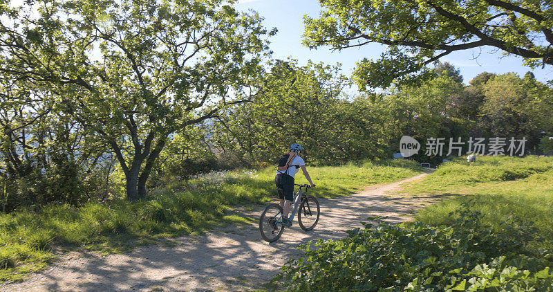 成熟的女人骑着电动自行车在森林的小路上行驶