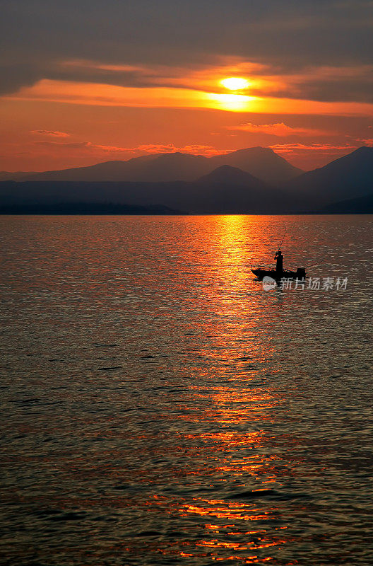 夕阳下的湖面上有一艘渔船的剪影