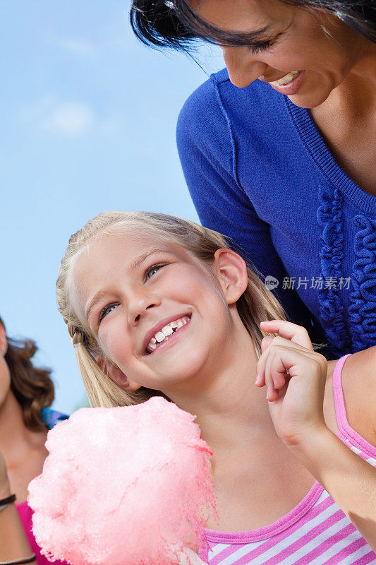 可爱的小女孩拿着棉花糖与家人在嘉年华