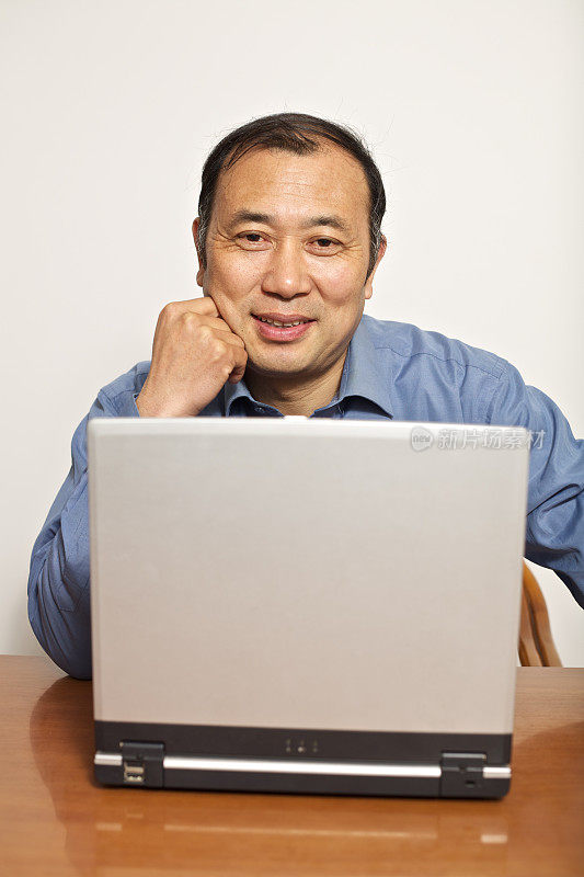 成熟的亚洲男人在家里用笔记本电脑