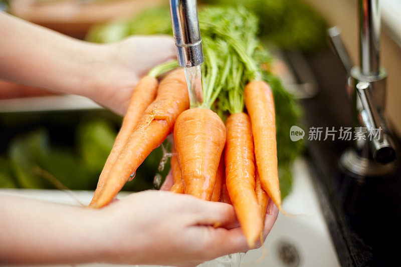 裁剪的女人在厨房里洗胡萝卜的图像