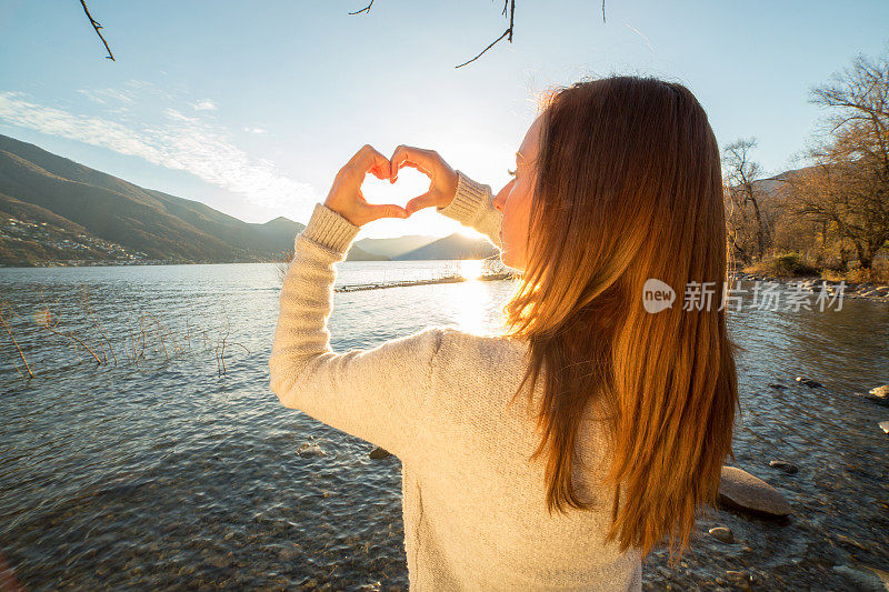 年轻女子在湖边做心形手指架