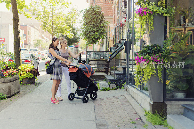 都市妈妈推着婴儿车和朋友逛街。