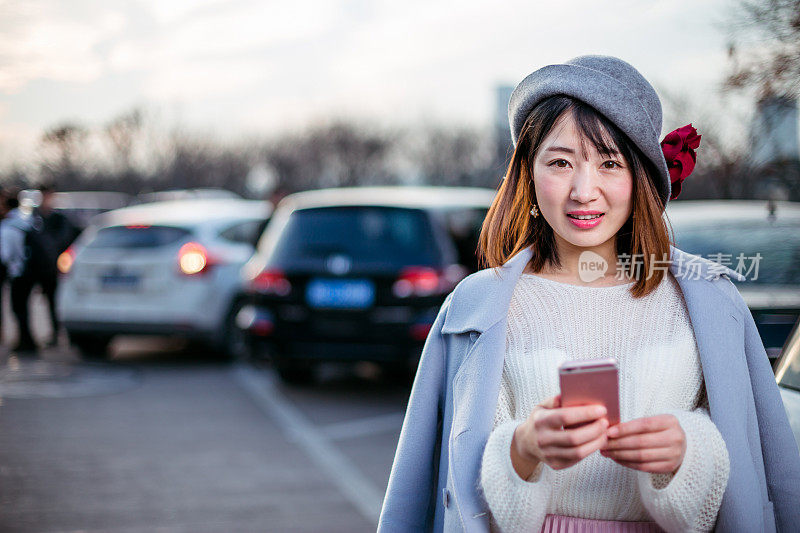 戴着帽子，穿着蓝色衣服的年轻女子在路上拿着手机