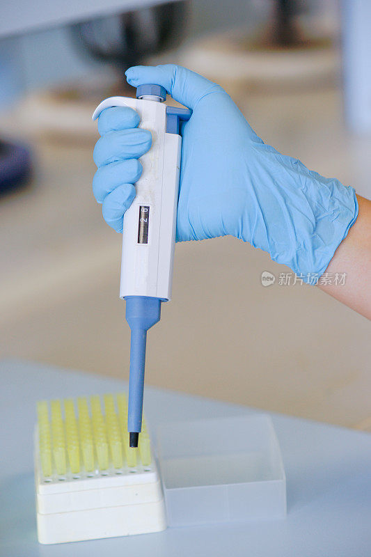 在化学实验室使用自动吸管工作的科学家。穿蓝色的手套。