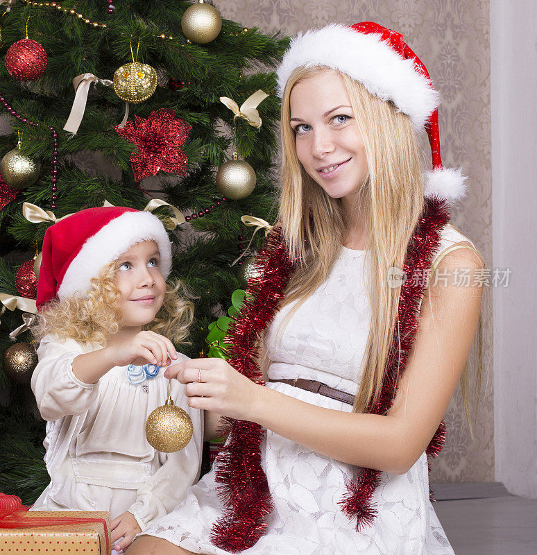 可爱的小女孩和她漂亮的妈妈戴着圣诞老人的帽子