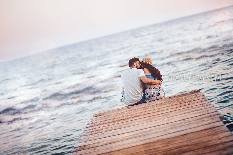 年轻的浪漫情侣度假坐在码头上亲吻