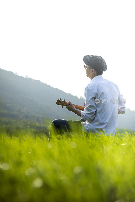 年轻男子在草坪上弹吉他的后视图