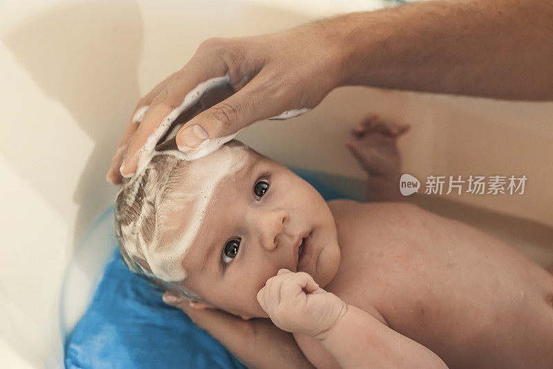 一个婴儿正在被他的父亲在家里用浴缸洗澡。