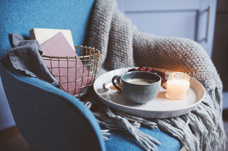 在家度过一个舒适的冬季周末。早上喝咖啡或可可，看书，暖和的针织毯子和北欧风格的椅子。Hygge概念。