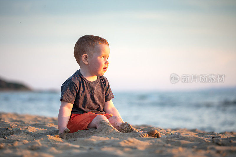 小男孩坐在海滩上看着太阳