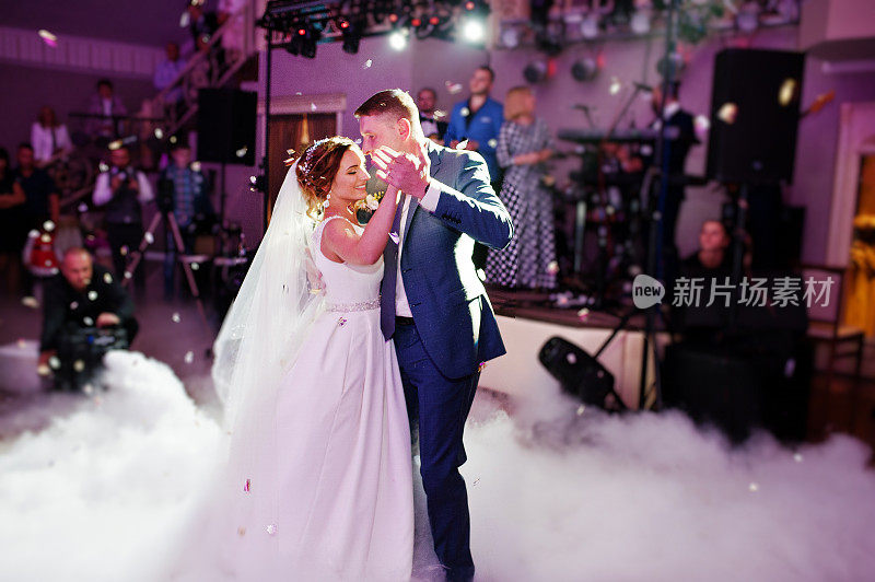 新婚夫妇在他们的婚礼上以浓重的烟雾和彩灯为背景跳舞。